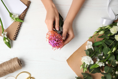 Florist holding beautiful leucospermum flower at white wooden table, top view