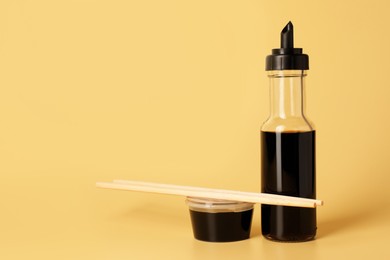 Photo of Soy sauce and chopsticks on yellow background, space for text