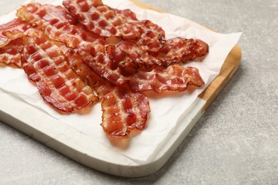 Photo of Board with fried bacon slices on grey textured table, closeup