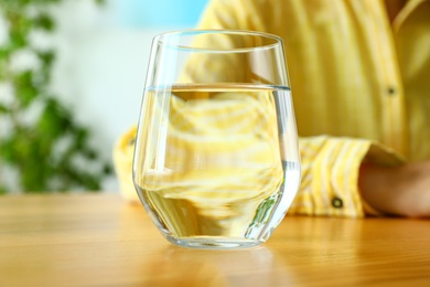 Photo of Woman and glass of water at wooden table, closeup. Refreshing drink