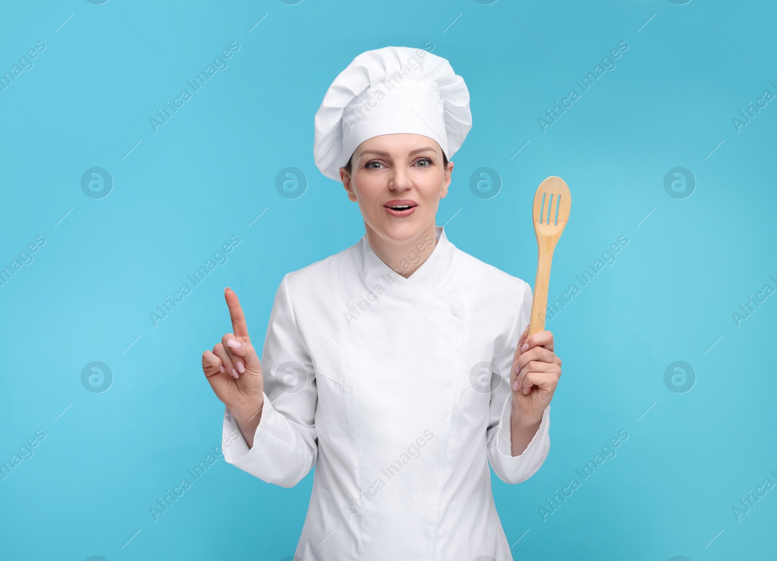 Photo of Happy chef in uniform holding wooden spatula on light blue background