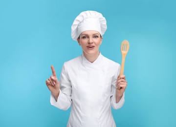 Happy chef in uniform holding wooden spatula on light blue background