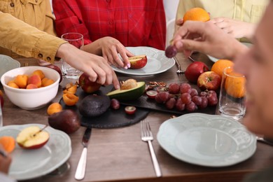 Photo of Vegetarian food. Friends eating fresh fruits at wooden table indoors, closeup