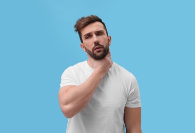 Photo of Man suffering from sore throat on light blue background. Cold symptoms