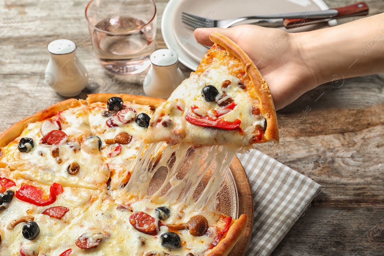 Photo of Woman holding slice of delicious hot pizza over table, closeup