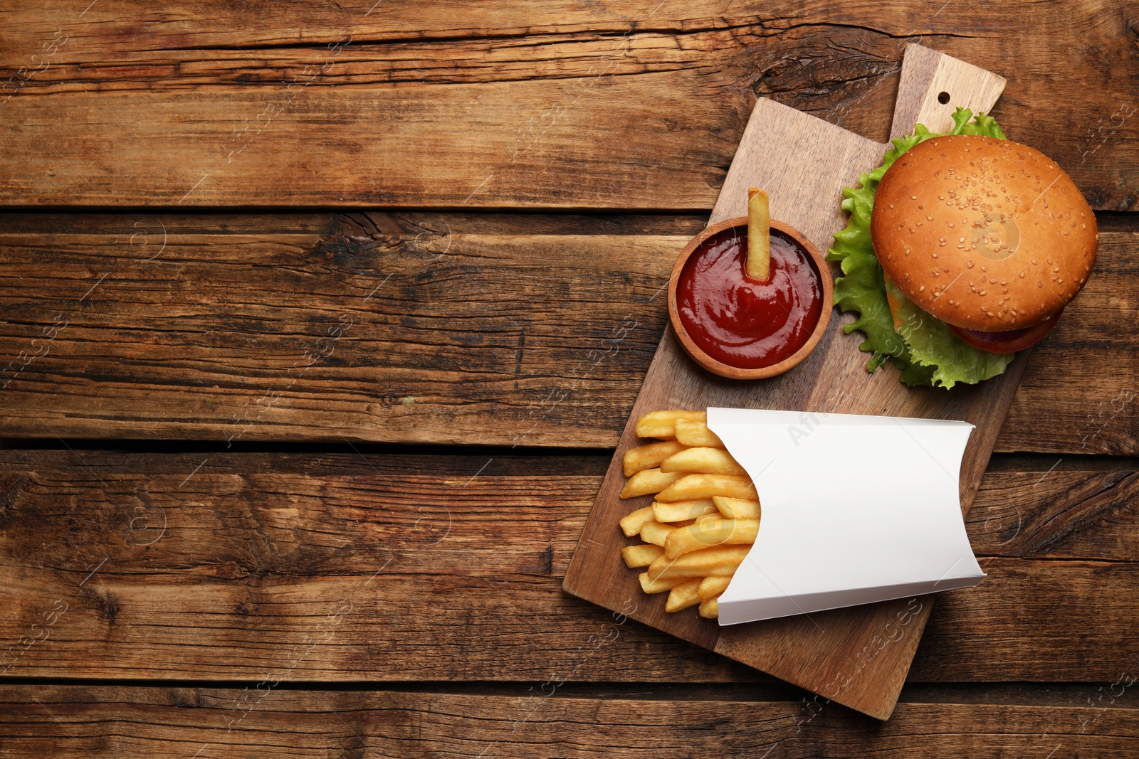 Photo of French fries, tasty burger and sauce on wooden table, top view. Space for text