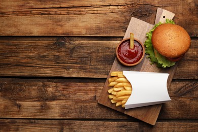 Photo of French fries, tasty burger and sauce on wooden table, top view. Space for text