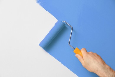 Man applying orange paint with roller brush on white wall, closeup