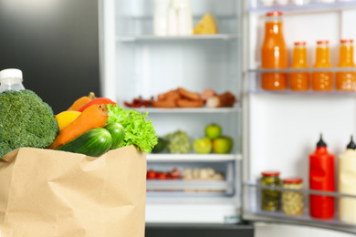 Photo of Paper bag full of products near refrigerator, closeup