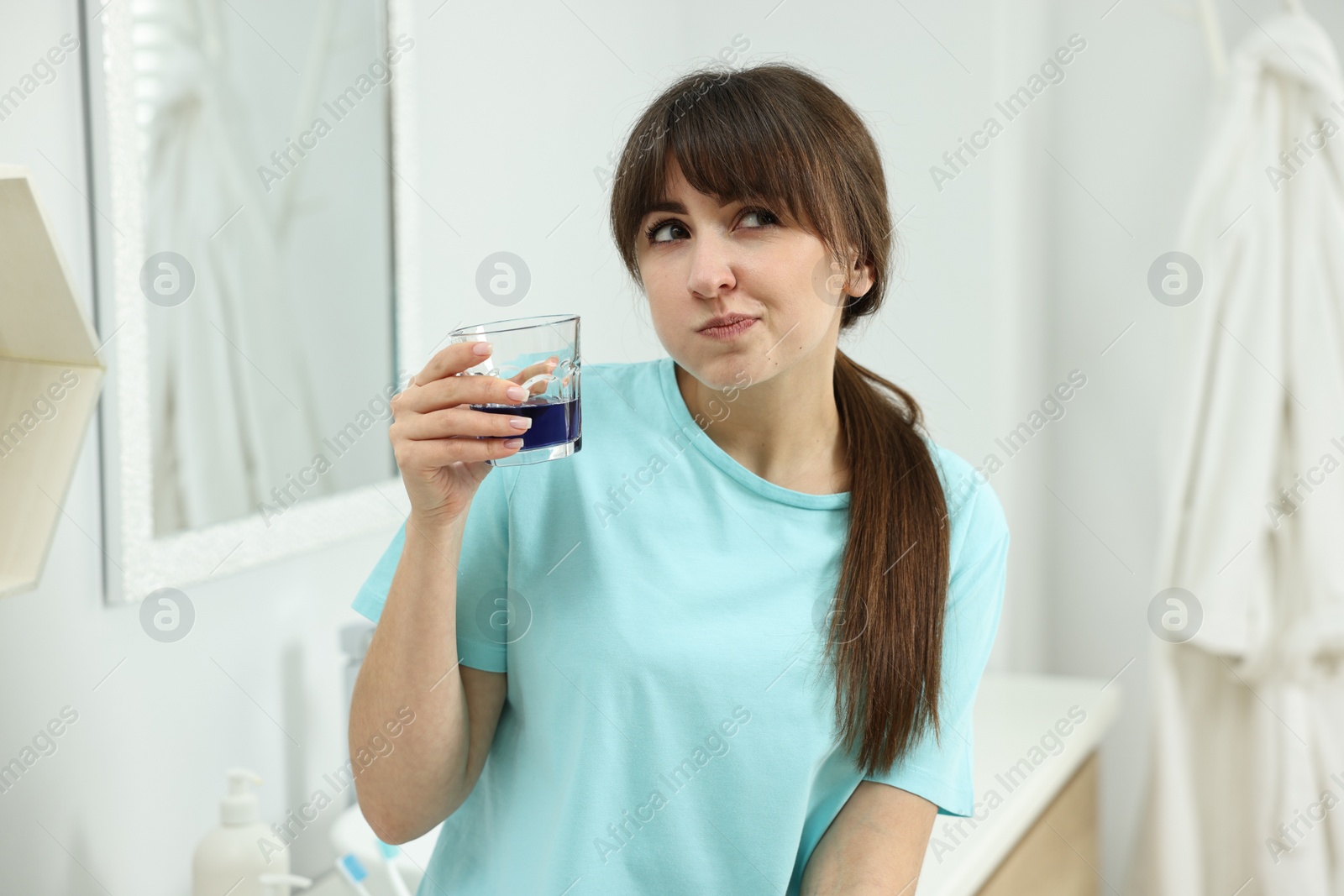 Photo of Young woman using mouthwash in bathroom. Oral hygiene