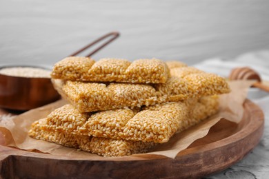 Wooden tray with delicious sweet kozinaki bars and sesame seeds on white table, closeup