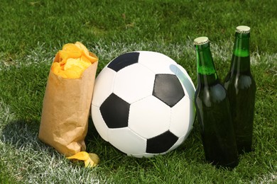 Photo of Football ball with beer and chips on green field grass