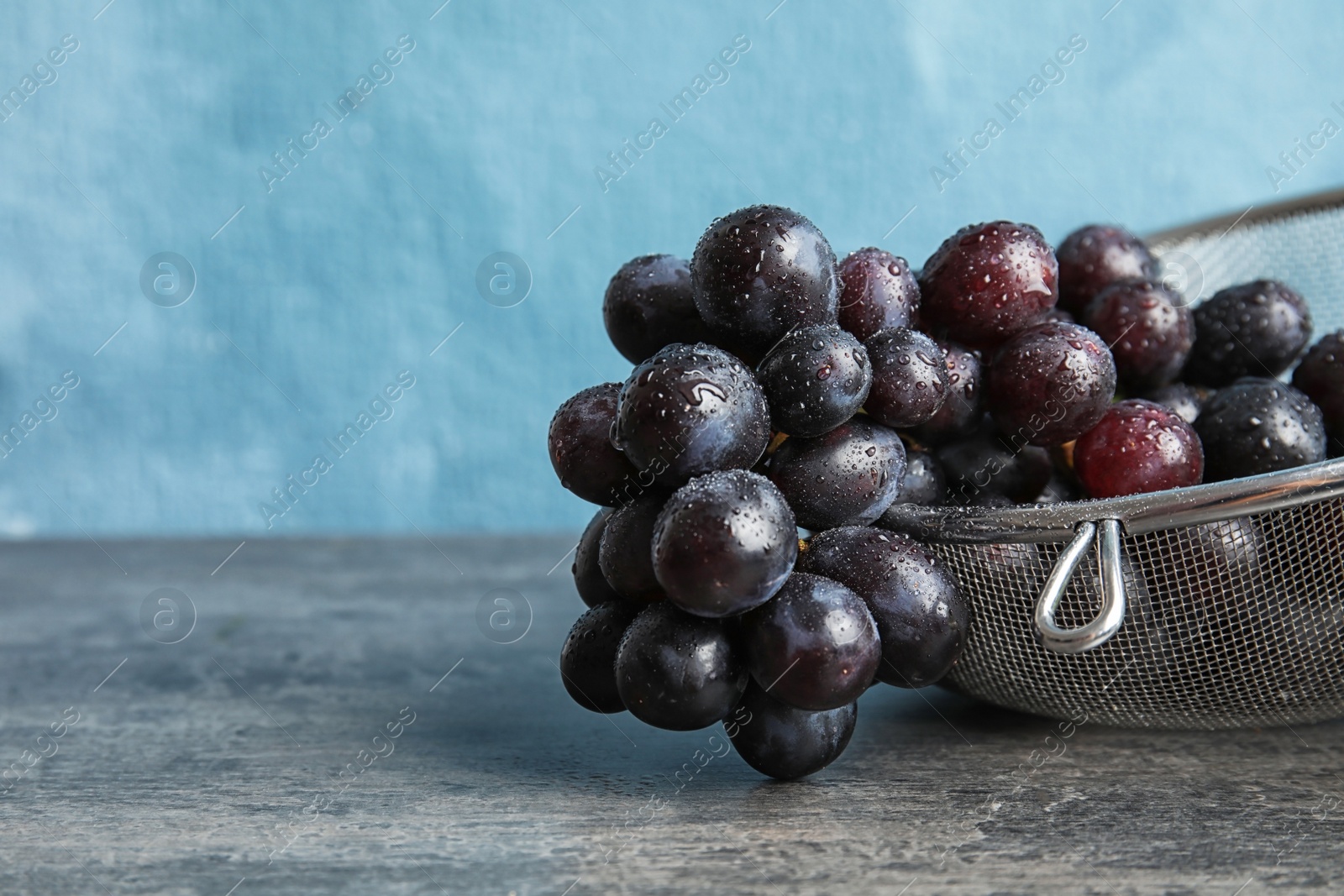 Photo of Fresh ripe juicy grapes in colander on table against color background with space for text