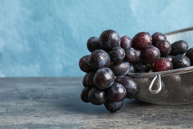 Photo of Fresh ripe juicy grapes in colander on table against color background with space for text