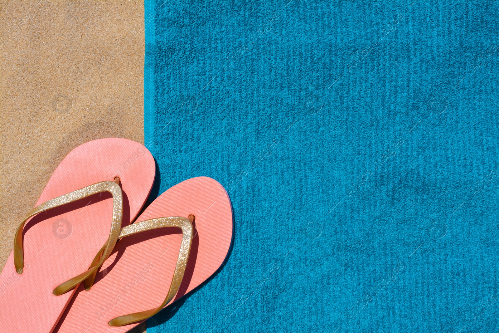 Photo of Soft blue beach towel with flip flops on sand, flat lay