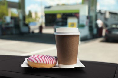 Photo of Paper coffee cup and doughnut on car dashboard at gas station