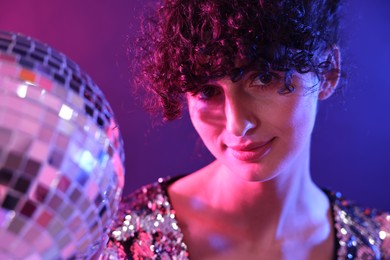 Beautiful young woman with disco ball posing on color background in neon lights