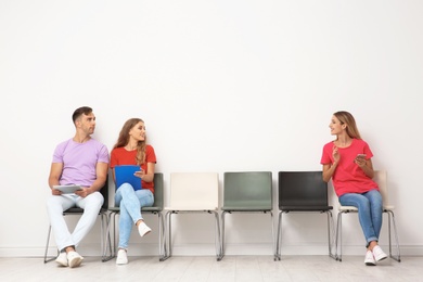 Group of young people waiting for job interview near light wall