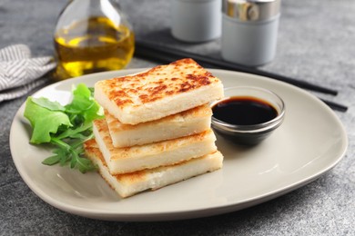 Photo of Delicious turnip cake with arugula and soy sauce served on grey table