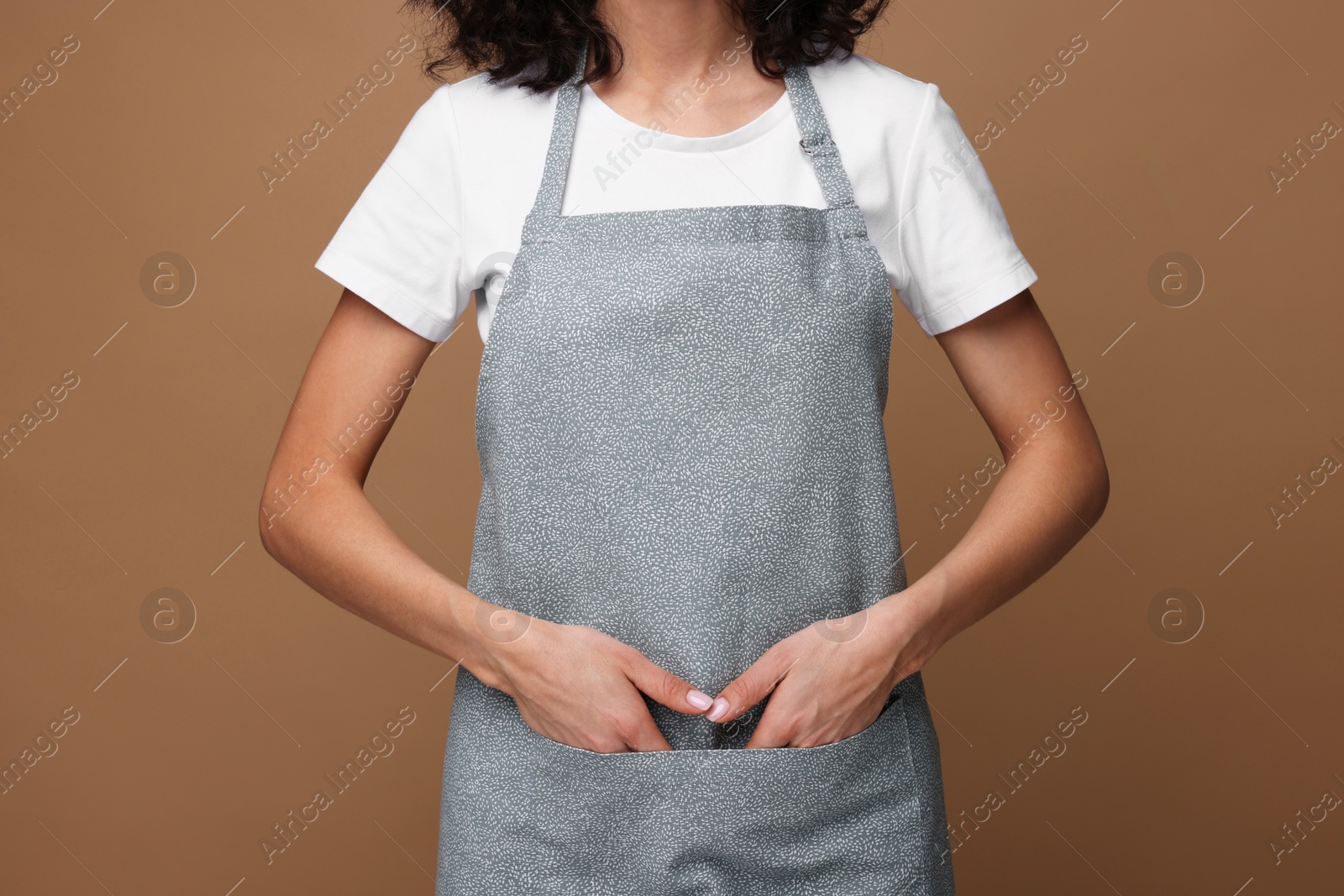 Photo of Woman wearing kitchen apron on brown background, closeup. Mockup for design