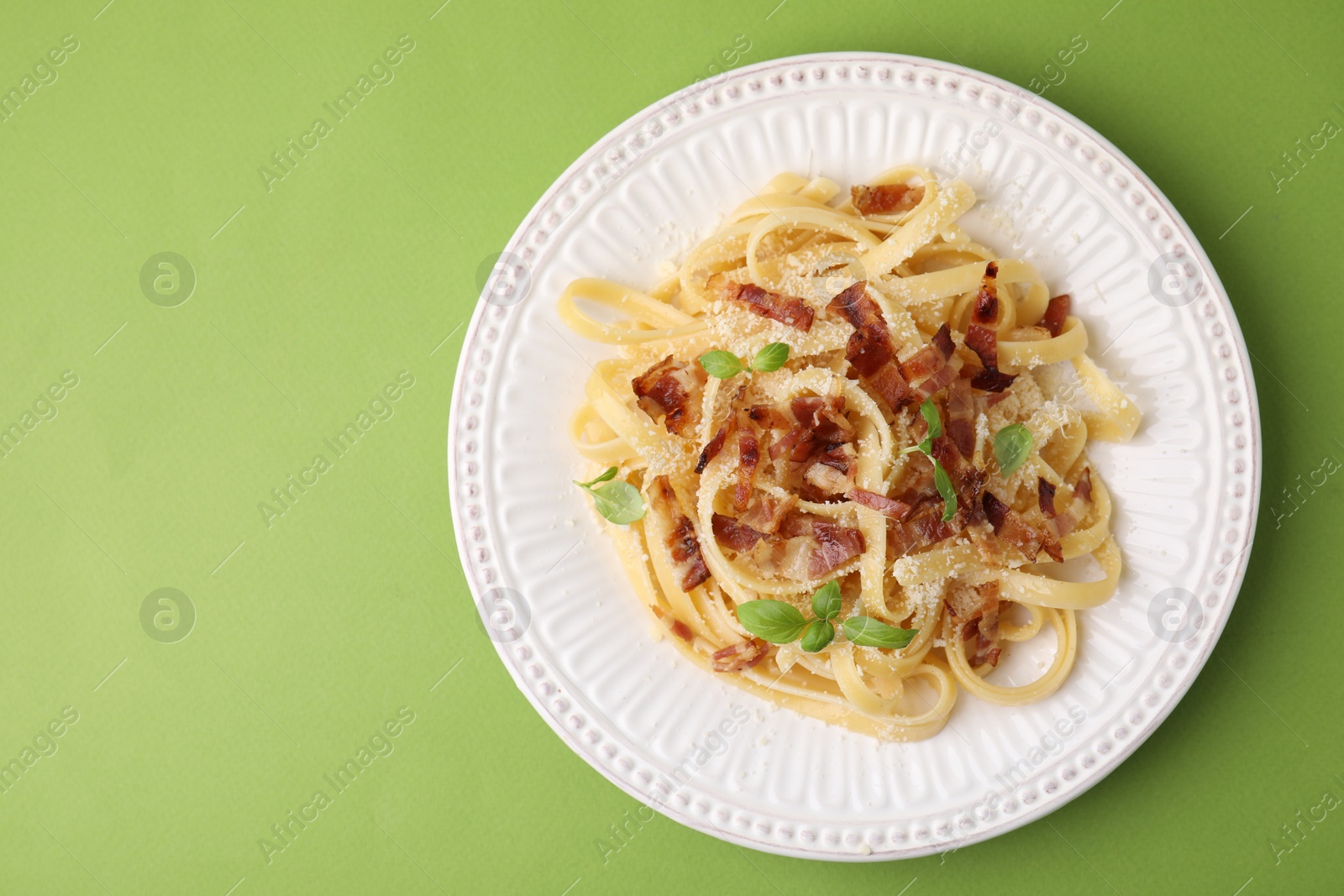 Photo of Tasty pasta with bacon and basil on light green table, top view. Space for text