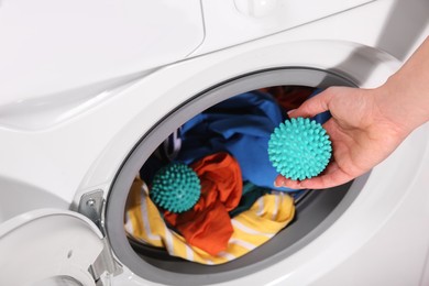 Photo of Woman putting green dryer ball into washing machine, closeup