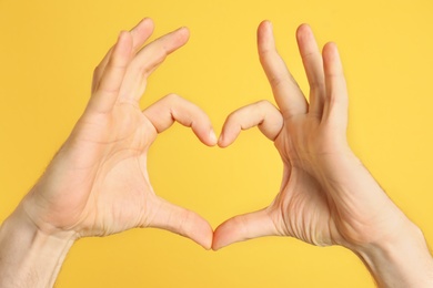 Photo of Man making heart with his hands on color background, closeup