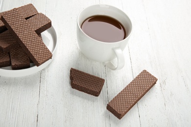 Photo of Plate of delicious chocolate wafers with cup of tea on white wooden background