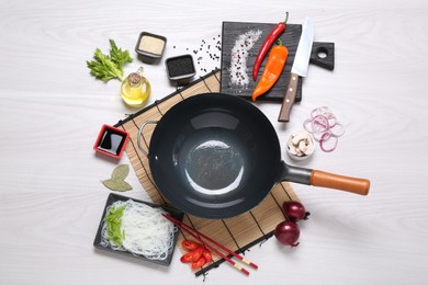 Wok, chopsticks and different products on white wooden table, flat lay