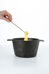 Photo of Woman dipping grape into fondue pot with tasty melted cheese on white background, closeup