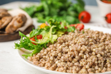 Photo of Tasty buckwheat porridge with salad on white wooden table, closeup