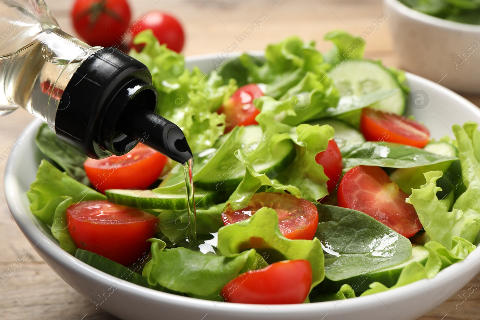 Photo of Pouring oil into delicious vegetable salad on wooden table, closeup