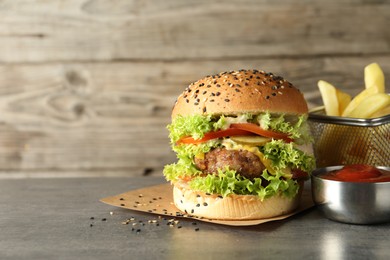 Photo of Burger with delicious patty, french fries and sauce on gray table, space for text