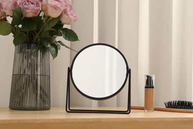 Photo of Mirror, foundation, brush and vase with pink roses on wooden dressing table