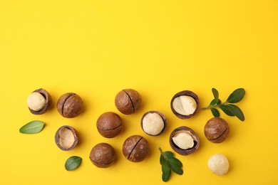 Photo of Tasty Macadamia nuts and leaves on yellow background, flat lay. Space for text