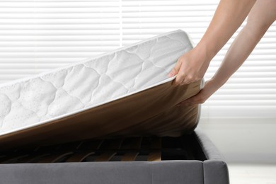 Photo of Woman putting soft light green mattress on gray bed indoors, closeup