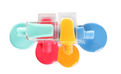 Photo of Spilled different nail polishes with bottles on white background, top view