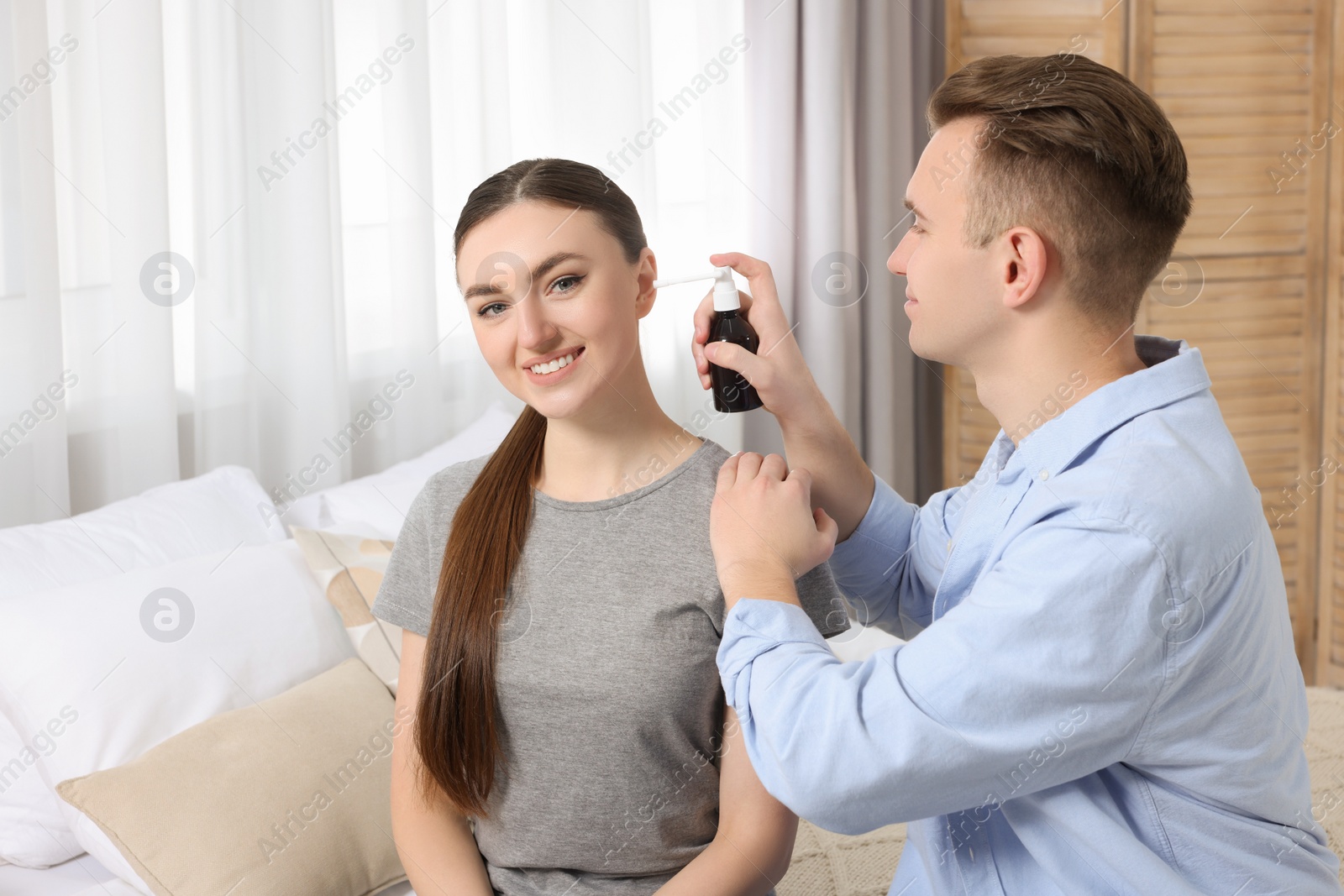 Photo of Man spraying medication into woman's ear at home