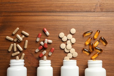 Overturned bottles with different dietary supplements on wooden table, flat lay. Space for text