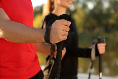 Photo of Couple practicing Nordic walking with poles outdoors, closeup