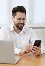 Handsome young man using smartphone at wooden table in office