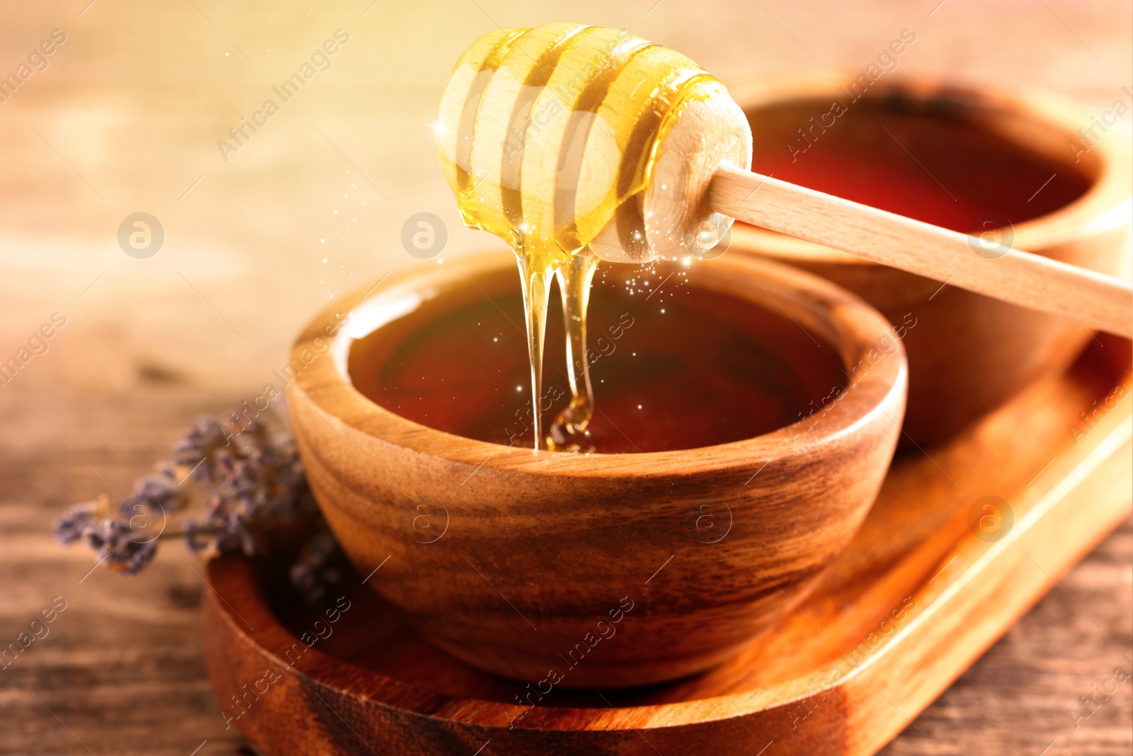 Image of Natural honey dripping from dipper into wooden bowl on table under sunlight, closeup