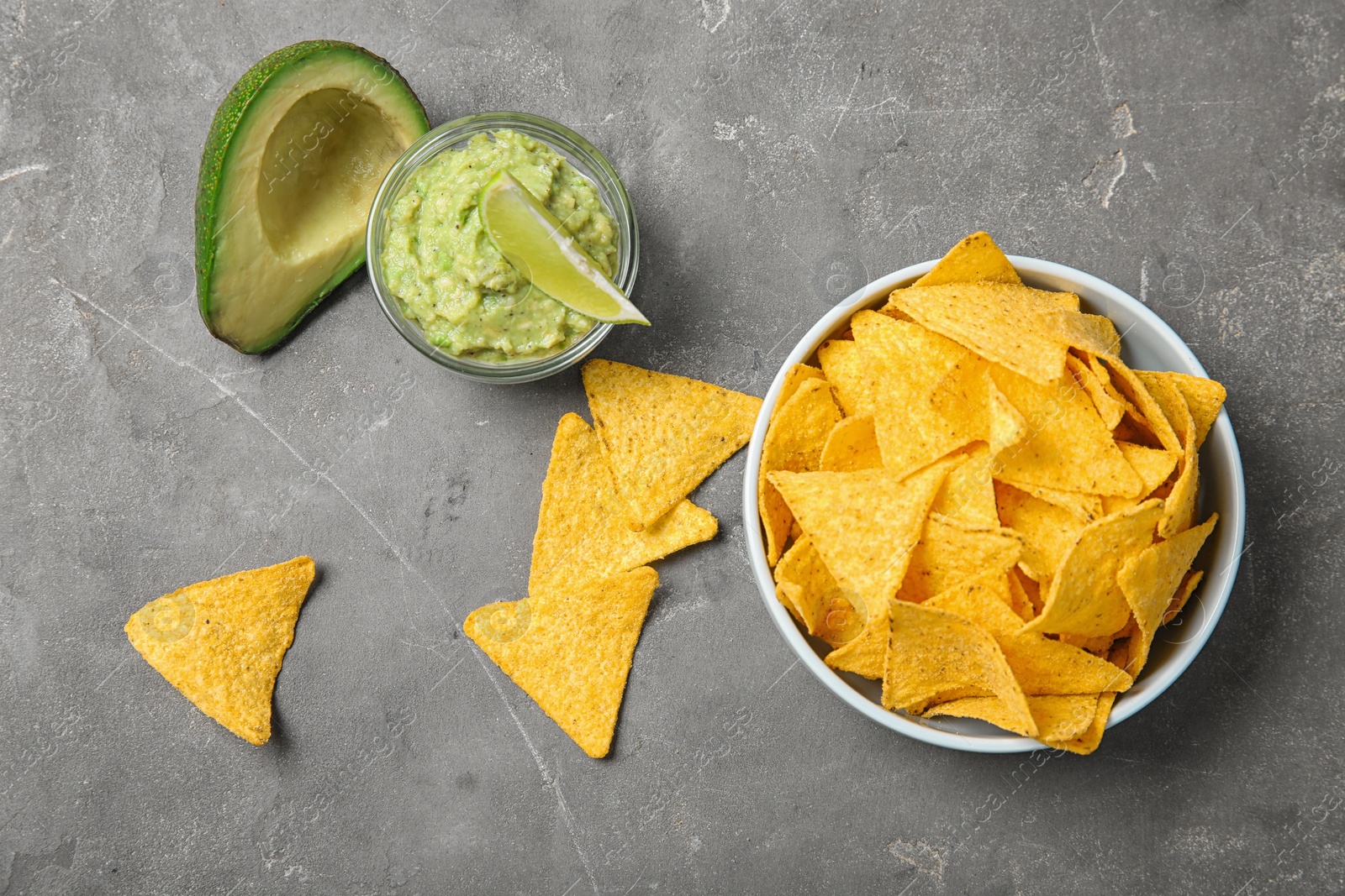 Photo of Delicious mexican nachos chips in bowl served with guacamole sauce and avocado on grey table, flat lay