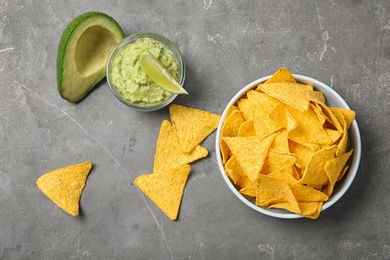 Delicious mexican nachos chips in bowl served with guacamole sauce and avocado on grey table, flat lay