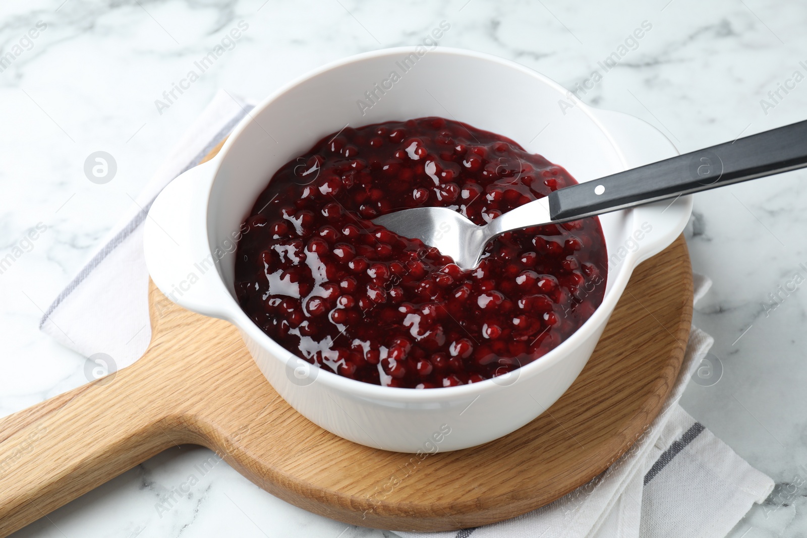 Photo of Fresh cranberry sauce in bowl served on white marble table, closeup