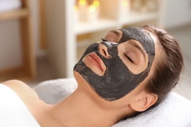 Beautiful woman with black mask on face relaxing in spa salon