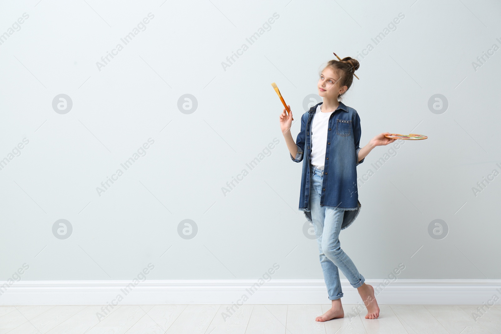 Photo of Little girl with brush and paint palette near light wall indoors. Space for text