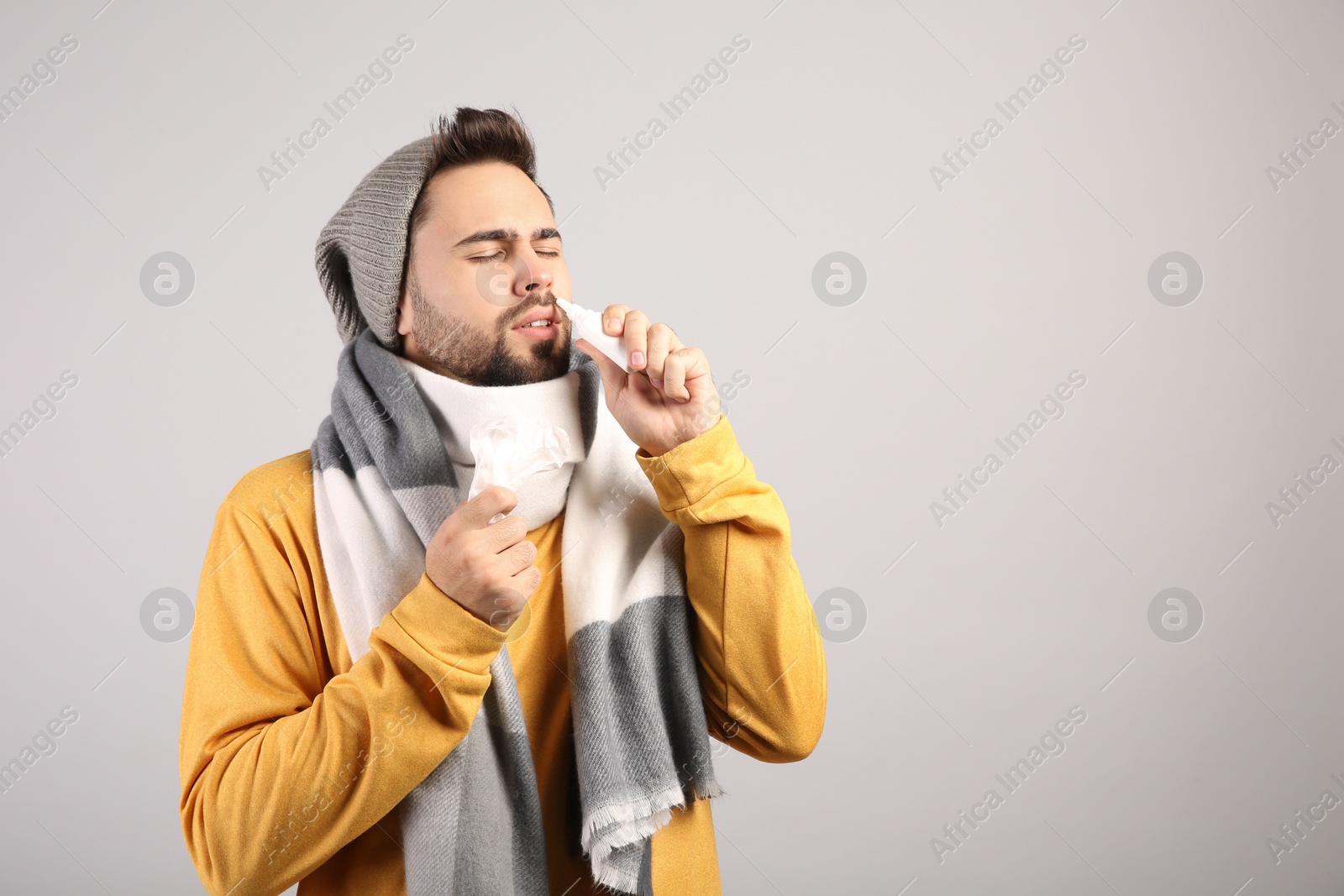 Photo of Man using nasal spray on light grey background, space for text