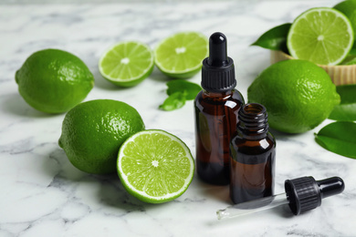 Photo of Lime essential oil and citrus fruits on marble table