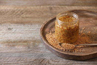 Jar and spoon of whole grain mustard on wooden table. Space for text